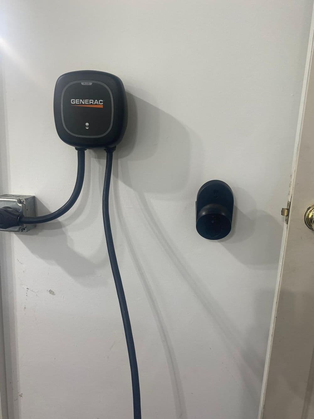 Generac EV charger mounted on wall with charging cable and wall socket.