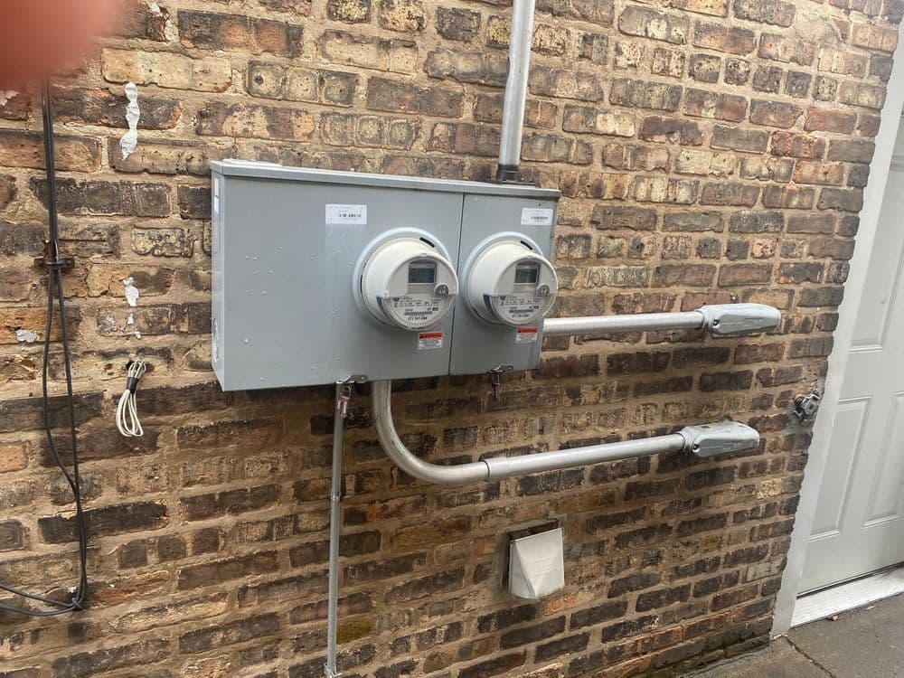 Two electric meters installed on a brick wall with metal conduit connections.
