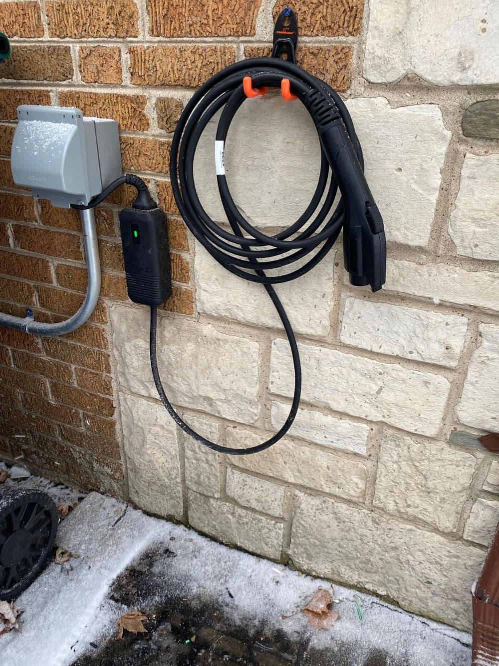Electric vehicle charging station with a coiled cable mounted on a brick and stone wall.