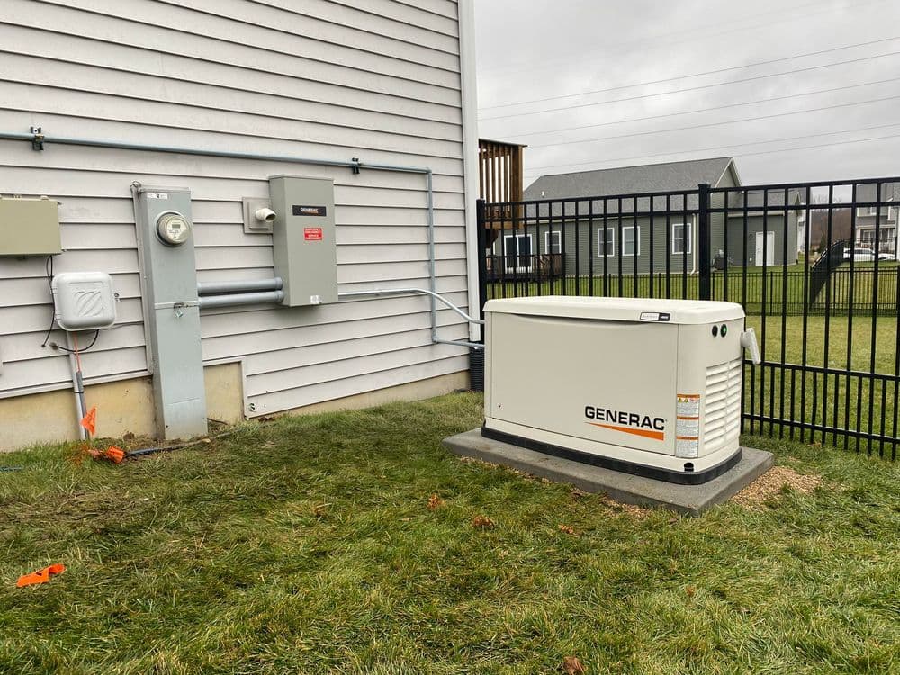 Generac generator installed outside a house near electrical panel and fenced yard.