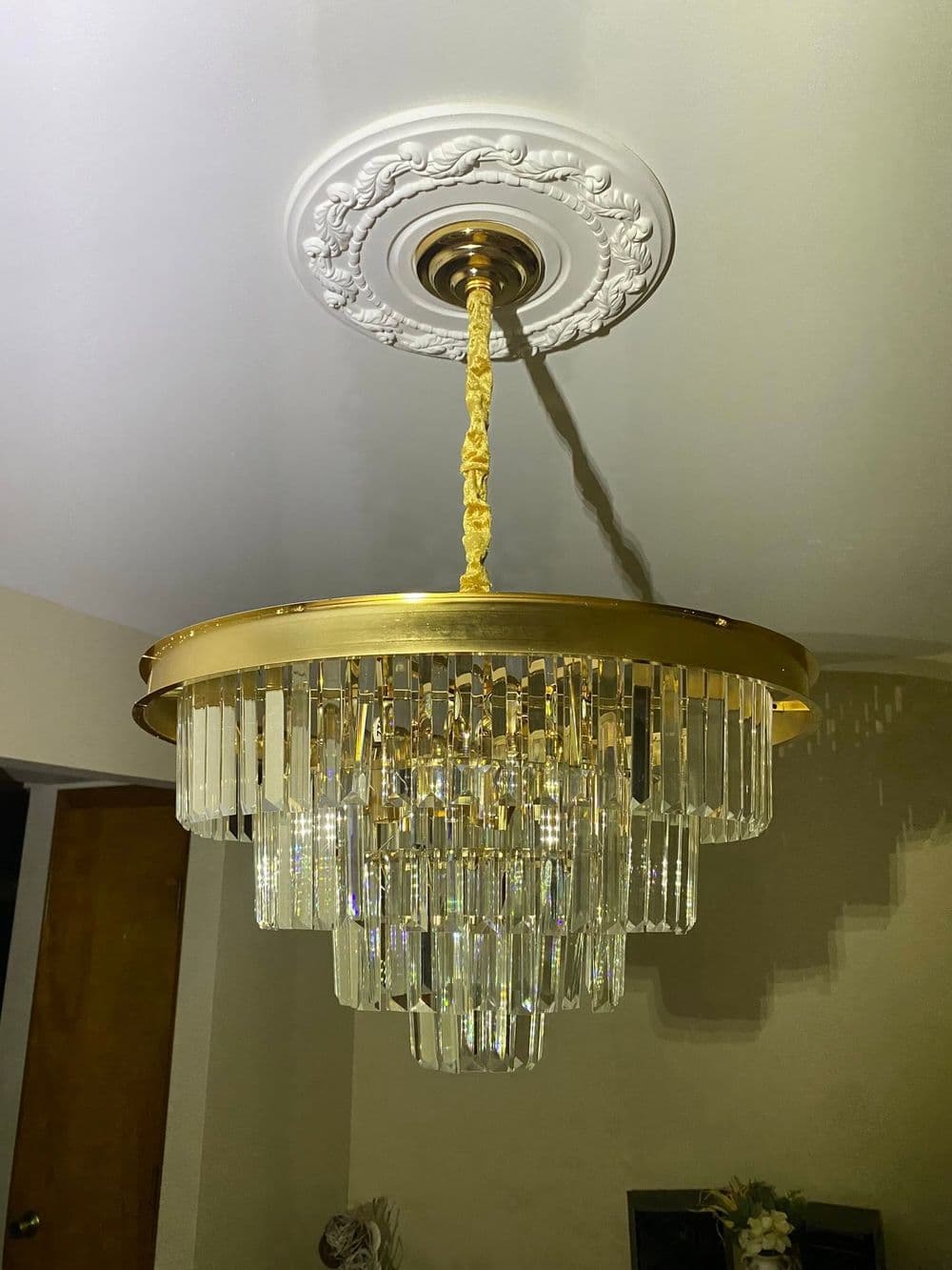 Elegant gold chandelier with crystal accents and ornate ceiling medallion. Bright interior lighting.