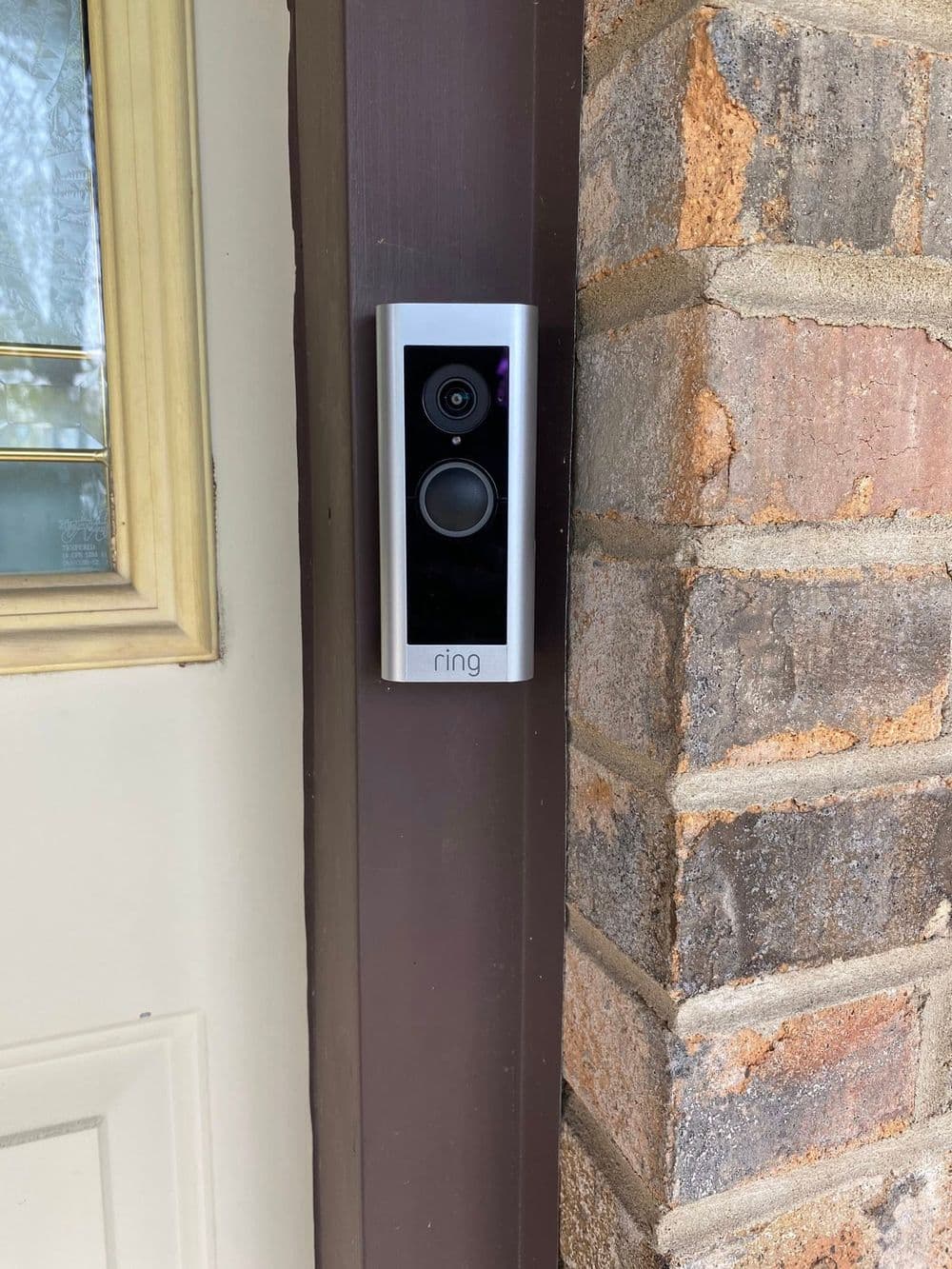 Ring video doorbell installed on a brick wall next to a wooden door for home security.