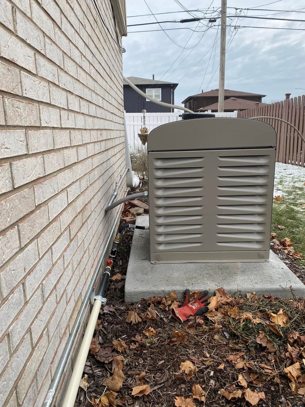 Generator unit beside a house, showing utility connections and surrounding landscaping in autumn.