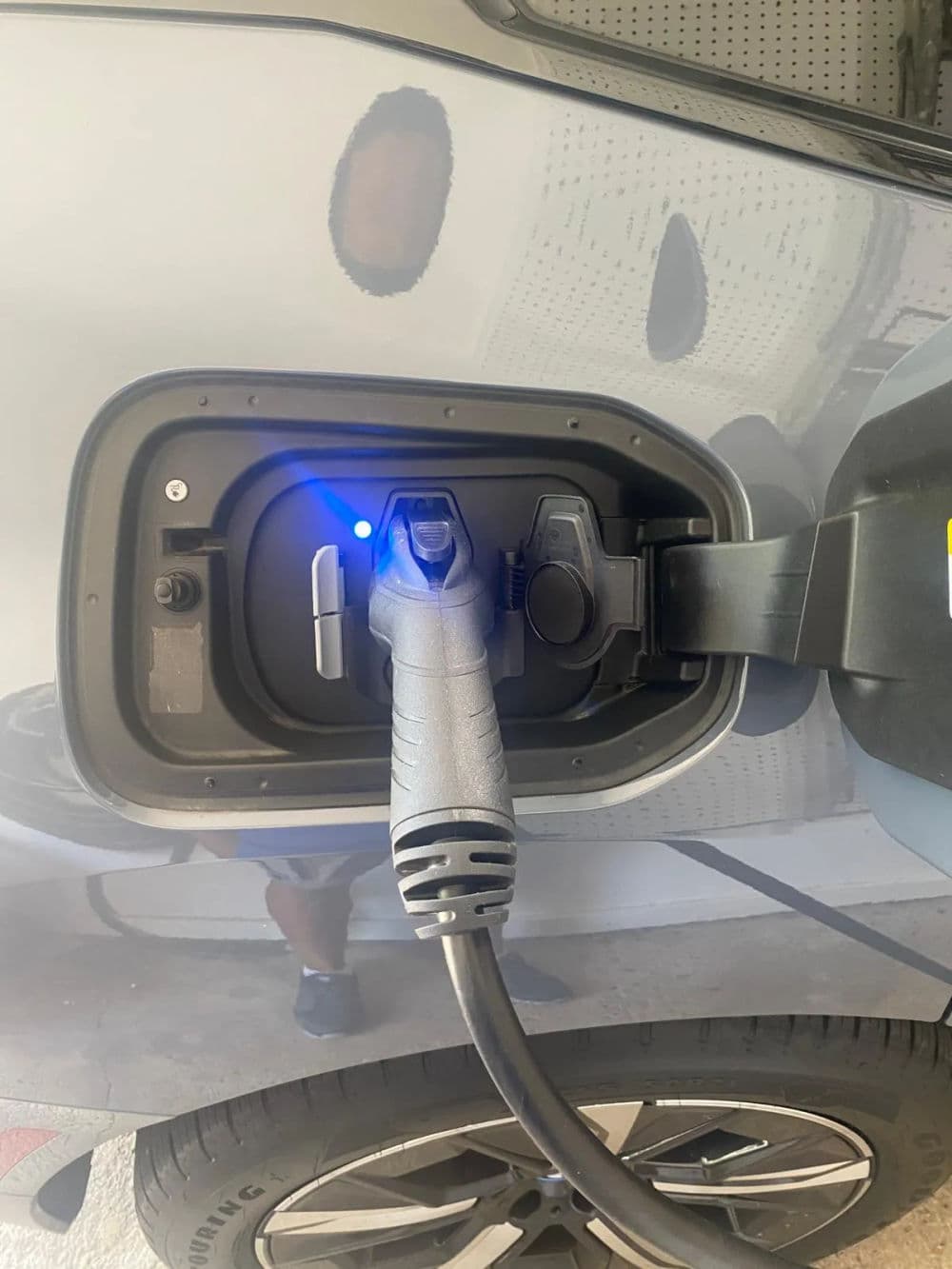 Electric car charging port with plugged-in connector and blue indicator light.