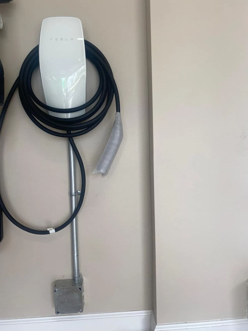 Tesla electric vehicle charging station mounted on a wall with coiled charging cable.