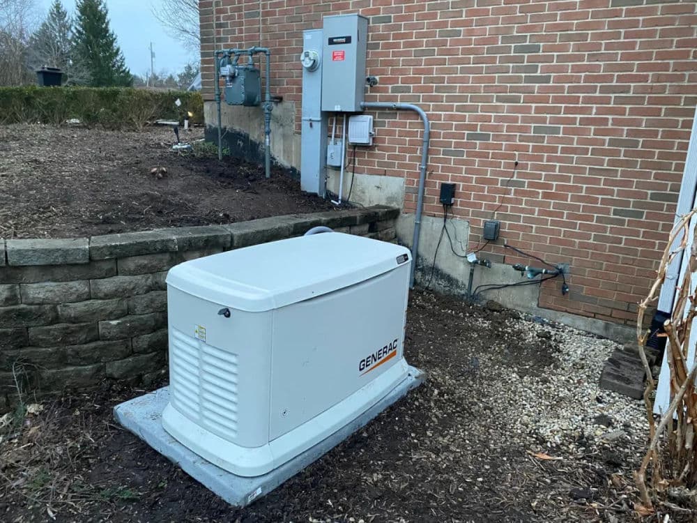 Home generator installation outside a brick house with utility connections and landscaping.