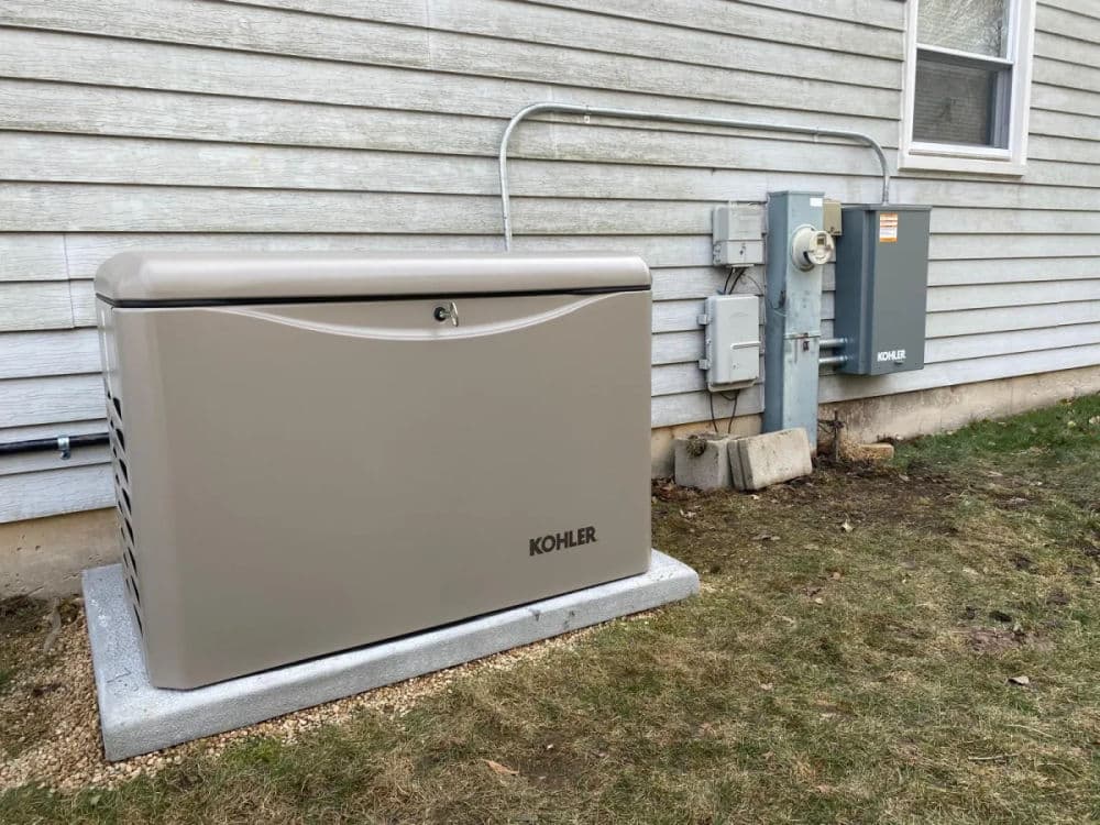 Kohler generator installed outside a home, next to an electrical panel on a grassy area.