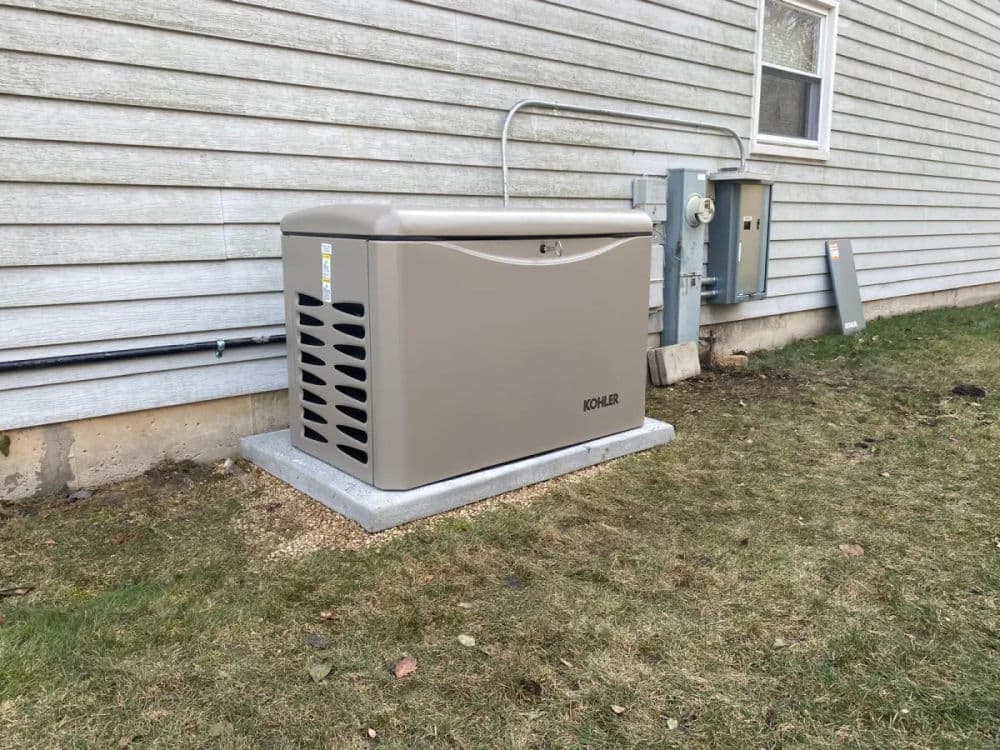 Kohler home generator installed on concrete pad beside a house with utility connections.