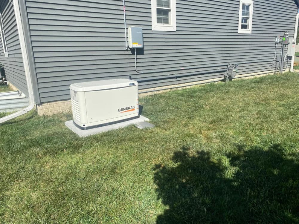 Generator installation outside a home, with control panel and grass surrounding the area.