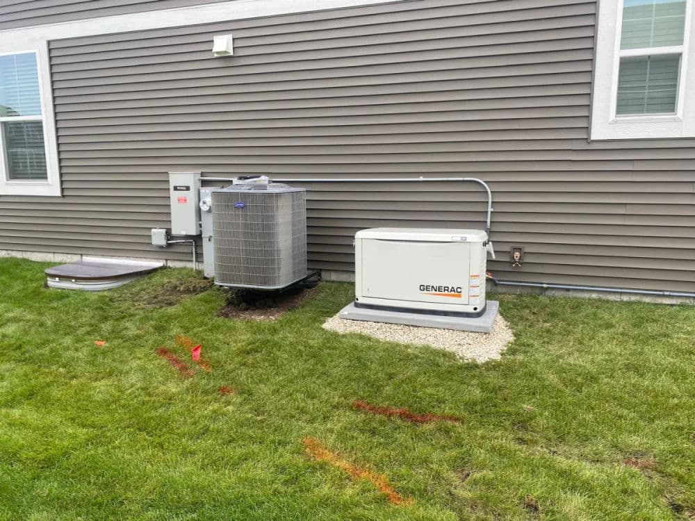 Air conditioning unit and Generac generator installed next to a house on green grass.