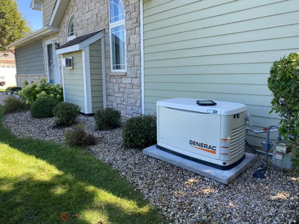Generac home generator installed beside a house with landscaped yard and stones.